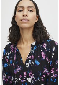 Blouse noire à motif floral, ornée de fleurs roses, bleues et blanches, avec un décolleté en V et un tissu léger, idéale pour un usage décontracté.