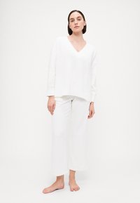 White loungewear set featuring a loose V-neck top and wide-leg pants. Soft, textured fabric with a relaxed fit and hems. No patterns or hardware.