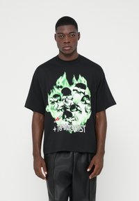 Tricou oversize negru cu un grafic verde ce prezintă cranii și flăcări. Designul din față include un text alb care spune " +TEAMGEIST" și un logo.