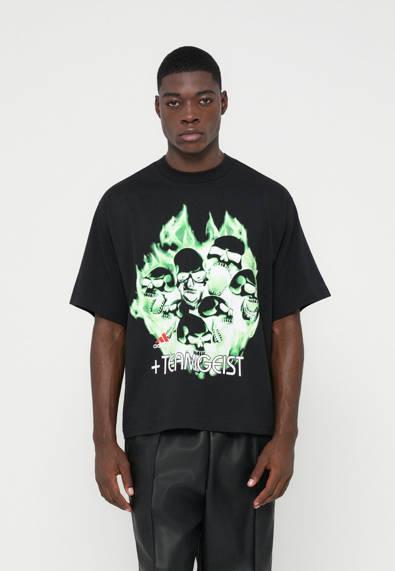 Tricou oversize negru cu un grafic verde ce prezintă cranii și flăcări. Designul din față include un text alb care spune " +TEAMGEIST" și un logo.
