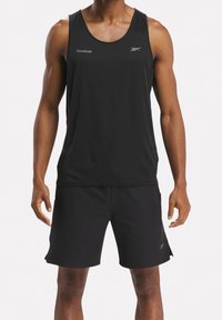 Černý sportovní tílko s kulatým výstřihem a průramky, v kombinaci s černými šortkami. Na obou kouscích se nachází malá značka Reebok.