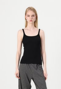Svart tettsittende tank top med smale stropper, rund halslinning og myk tekstur. Kombinert med horisontalt stripete bukser i svart og grått.