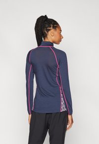 Marineblå langermet genser med rosa detaljer og blomstrede sidelommer. Har høy krage og slim fit, laget av lett, teksturert materiale.