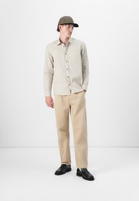 Lys rutete skjorte, beige chinos og svarte loafers komplementert av en rutete caps. Enkelt, skreddersydd design med nøytrale farger.