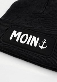 Black knit beanie featuring a rectangular patch with the word "MOIN" in bold white letters and an anchor graphic. Soft texture, casual design.