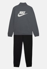Survêtement Nike composé d'une veste zippée grise avec un grand logo blanc dans le dos et un pantalon noir à taille élastique. Texture de tissu douce.