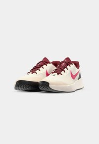 Sneakers med en kremfarget mesh-overdel, maroon detaljer, rosa logo og svart gummisåle; har snøring og teksturert materiale.