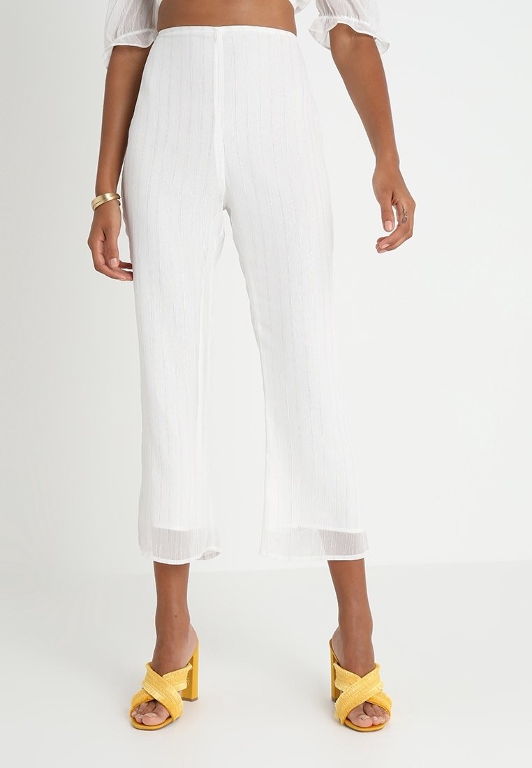 Białe plisowane spodnie o skróconym kroju z delikatnym połyskiem, charakteryzujące się prostym krojem i długością do kostek. Zestawione z żółtymi sandałami na słupku.
