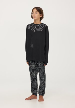 Maglietta nera a maniche lunghe con design di ragnatela e ragno bianchi, abbinata a pantaloni neri con un motivo a ragnatela ripetuto.