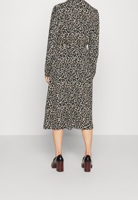 Woman wearing a black midi dress with white and beige abstract print, long sleeves, and black heeled shoes, standing against a plain background.