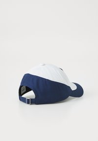 Cappellino da baseball con parte anteriore bianca e retro blu navy, realizzato in cotone. Cinturino regolabile sul retro, con un bottone sulla parte superiore.