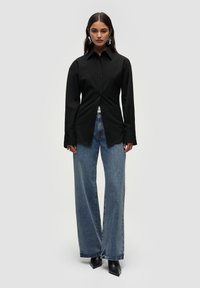 Sort langærmet skjorte med knaplukning og spids krave, parret med løse blå denim jeans og spidse sorte hæle.