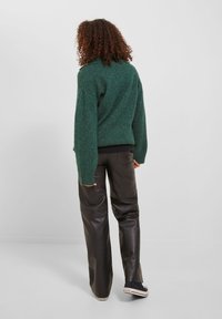Maglione verde in lana con collo alto e maniche oversize, abbinato a pantaloni in pelle neri e sneakers nere. Tessuto testurizzato.