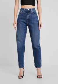 Korkeavyötäröiset, suorat siniset farkut, joissa haalistettu pesu, viisi taskua ja vaaleat saumat. Varustettu napin suljennalla ja vyölenkeillä.