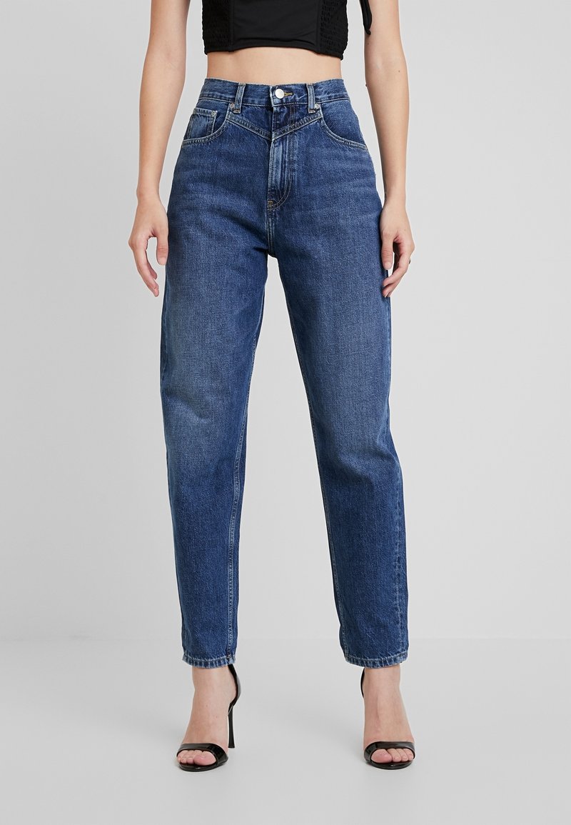 Korkeavyötäröiset, suorat siniset farkut, joissa haalistettu pesu, viisi taskua ja vaaleat saumat. Varustettu napin suljennalla ja vyölenkeillä.