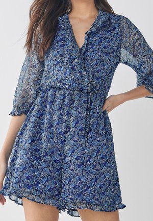 Robe à imprimé floral bleu en tissu transparent. Elle présente un col, de longues manches bouffantes et un ourlet rufflé avec une taille cintrée.