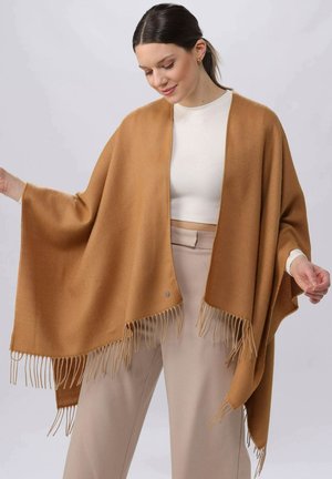 Camel-colored wrap made of soft material, featuring a loose shape, fringe detail along the hem, and an accent button near the front.