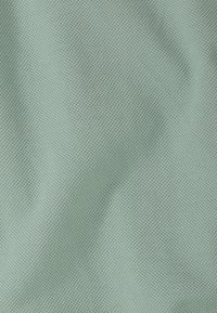 Tissu texturé en vert doux et atténué, présentant un motif fin et tissé. La surface paraît lisse avec une légère variation dimensionnelle.