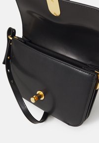 Borsa a tracolla in pelle nera con finitura liscia, hardware dorato, chiusura a scatto frontale e tracolla regolabile. Interno con texture.