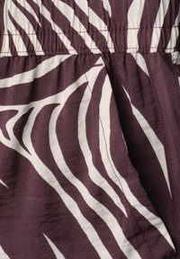 Gros plan d'un tissu à rayures zèbre blanches et violet foncé avec des coutures visibles, montrant une section froncée et une partie de l'ouverture de la poche.