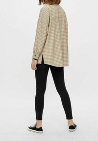 Ljusbeige rutig skjorta med sänkta axlar, sidofickor och knäppta ärmslut; matchad med svarta skinny jeans och svarta sneakers.