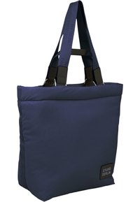 Marineblå totebag i stoff med avtakbare stropper, med firkantet form, jevn tekstur, og et rektangulært patch med "STUDIO BERLIN"-logo.
