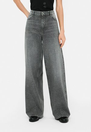 Grijze denim broek met ruime pijpen, versierd met studs, hoge taille en vijf zakken. De stof heeft een gladde textuur met metallic accenten.