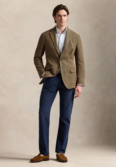 Rjavi blazer z vinskimi ribicami in strukturiranimi rameni, kombiniran s svetlo modro in belo črtasto srajco, temno modrimi hlačami in opremljenimi svetlo rjavimi loaferji.