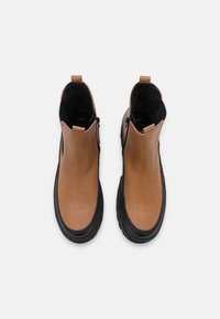 Bottines en cuir marron avec une finition lisse, semelles en caoutchouc noires, fermetures éclair sur le côté et accents texturés noirs en haut.
