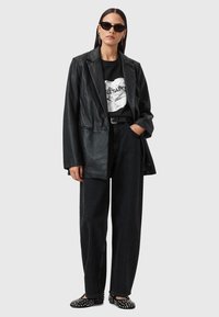 Blazer di pelle nera sopra una t-shirt grafica nera, abbinato a jeans neri a vita alta e scarpe flat con borchie. Gli occhiali da sole completano il look.