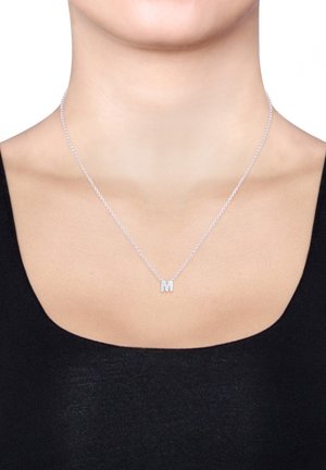 Silver necklace with a thin chain and a block-letter "M" pendant, resting on a black garment against a neutral background.