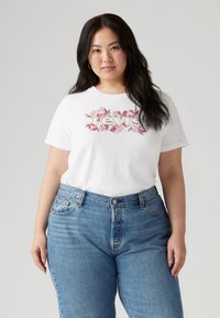 Λευκό κοντομάνικο t-shirt με λουλουδάτο σχέδιο λογότυπου Levi's· συνδυασμένο με ψηλ όμεσα ανοιχτόχρωμα τζιν παντελόνια με ξεθωριασμένο φινίρισμα.