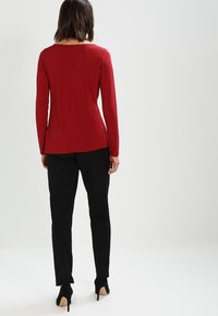 Rotes Langarmshirt mit Rundhalsausschnitt, kombiniert mit schwarzer Slim-Fit-Hose und schwarzen hohen Schuhen. Glattes Gewebe; schlichtes Design.
