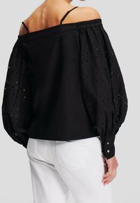 Svart off-shoulder blus med texturerade, puffade ärmar som har urklippta detaljer, avslutad med knäppningar vid ärmsluten och en slät kropp.