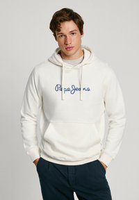 Felpa bianca realizzata in morbido tessuto, con logo "Pepe Jeans" ricamato in blu sul petto e tasca frontale. Abbinata a pantaloni blu navy.