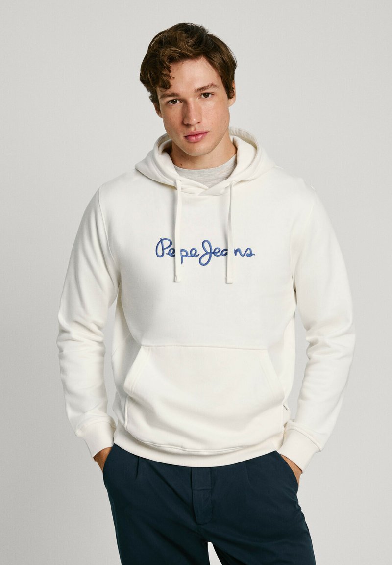Felpa bianca realizzata in morbido tessuto, con logo "Pepe Jeans" ricamato in blu sul petto e tasca frontale. Abbinata a pantaloni blu navy.