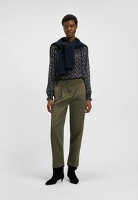 Blusa a righe navy con polsini elasticizzati, pantaloni verde oliva con pieghe e stivali neri alla caviglia con punta appuntita.