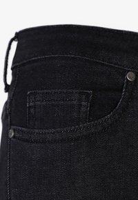 Černé džíny z denimu s přiléhavým střihem, jemnou texturou, malou zadní kapsou a kovovými detaily na pásku.