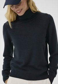 Navy turtleneck sweater with long sleeves, soft material, and ribbed neckline. Smooth texture with fitted design.