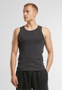 Graues Baumwoll-Tanktop mit Rundhalsausschnitt und weiten Armlöchern. Glatte Textur, taillierter Schnitt, kombiniert mit karierten schwarzen Shorts.