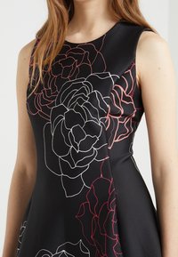 Svart ärmlös klänning med stora ros-mönster i vitt och rosa, tillverkad av ett mjukt tyg med en figurnära överdel och utsvängd kjol.