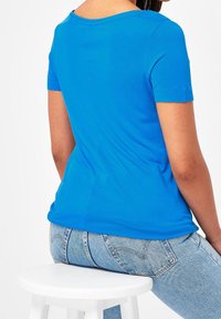 Blå kortærmet T-shirt i blødt materiale med rund halsudskæring, tætsiddende form og syede sømme, båret med lyseblå jeans.