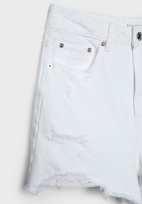 Short en denim blanc délavé avec ourlet effiloché, poche avant avec rivets, passants de ceinture et fermeture par bouton visible sur le côté droit.