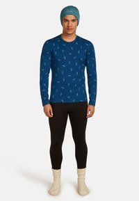 Modrá dlouhá košile s tyrkysovými vzory, černé legíny a krémové pletené ponožky, doplněné světle modrou čepicí.