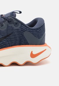 Marineblå sportsko med åndbart mesh-øvre, orange detaljer, polstret hvid sål og sort Swoosh-logo på siden.