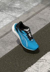 Scarpa da corsa leggera con tomaia in mesh blue, accenti neri, suola bianca e strisce riflettenti argento. Suola in gomma testurizzata per una migliore aderenza.
