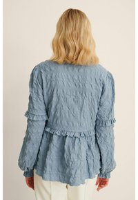 Helltürkise, strukturierte Bluse mit langen Ärmeln, Rüschendetails am Saum und an den Bündchen, mit einem lockeren, gestuften Design.