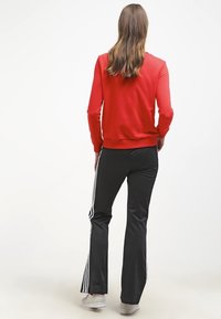 Röd sweatshirt med rundad halsringning, kombinerad med svarta byxor med vita sidostripes. Slät textur, avslappnad passform. Vita sneakers.