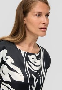 Zwarte blouse met witte abstracte patronen, voorzien van een ronde halslijn en een zachte stofstructuur, die een modern ontwerp benadrukt.