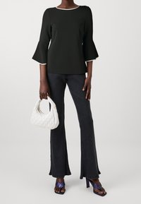 Černý top s vydutými rukávy a bílými detaily, spárovaný s tmavými žebrovanými kalhotami, držící bílou prošívanou kabelku a oblečený v purpurových sandálech na podpatku.